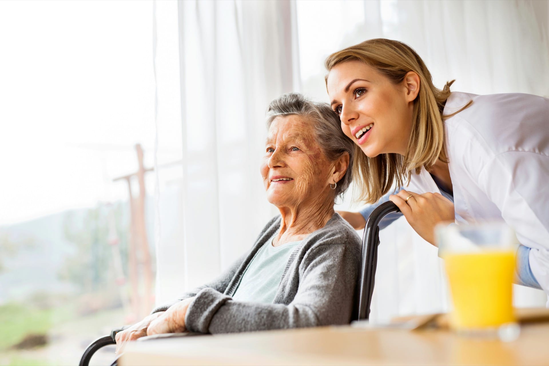 A caregiver smiling warmly with an elderly patient by a sunlit window